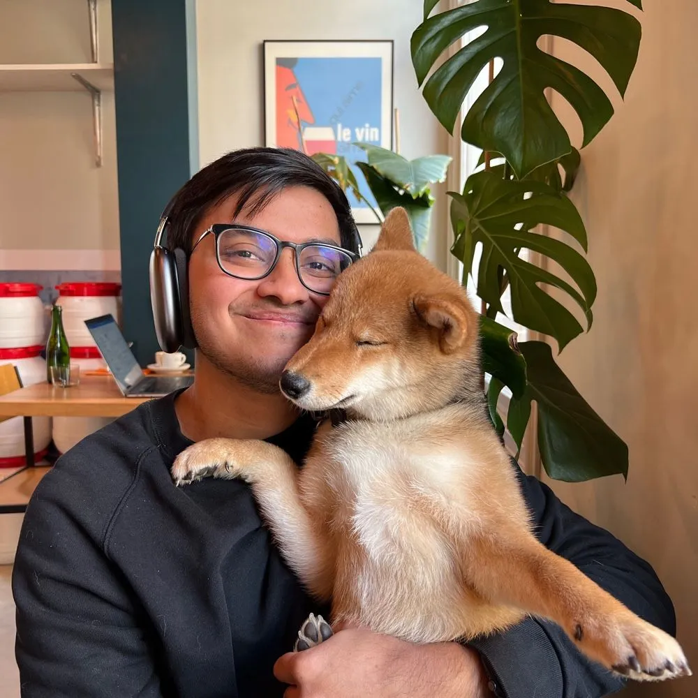 A photo of Amrith and his shiba inu dog named Sando in a cozy café in Amsterdam with a beautiful plant and random artwork in the background.