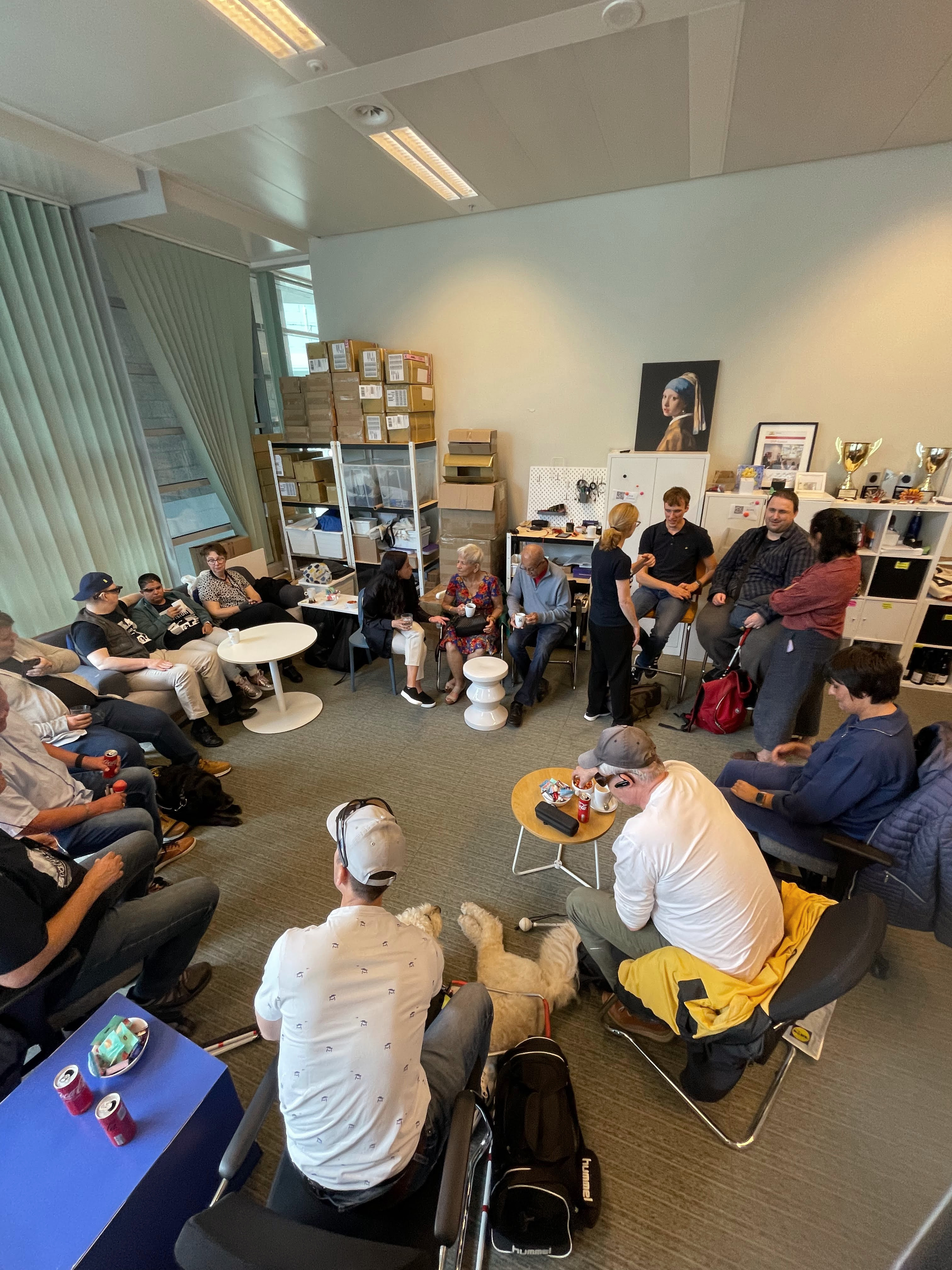 Envision community members and founders gather in a circle in an office, chatting over drinks, with dogs resting among the chairs.