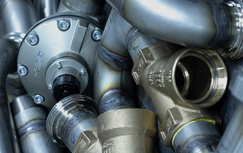 Close-up of metallic industrial pipes and fittings with threaded connections and a valve mechanism.