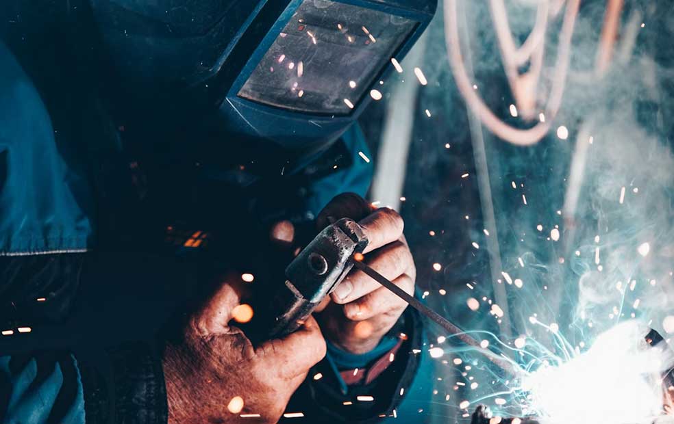 Close-up of a welder wearing a protective helmet and welding gloves, working with sparks flying around.