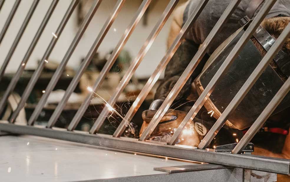 Person wearing protective gloves and welding mask welding metal bars with sparks flying.