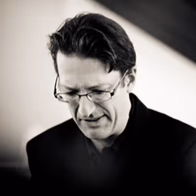 A man with glasses is playing a piano