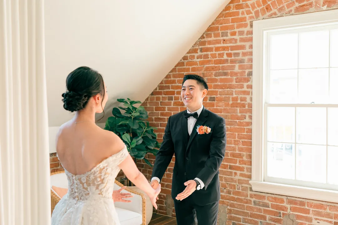 Groom smiling at the bride beside a loft window