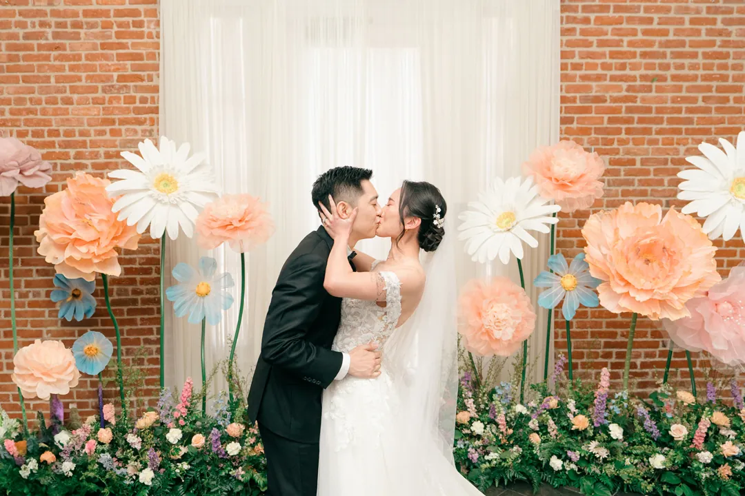 Couple kissing before a colorful floral backdrop