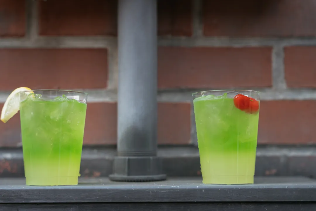 Two bright green drinks garnished with fruit