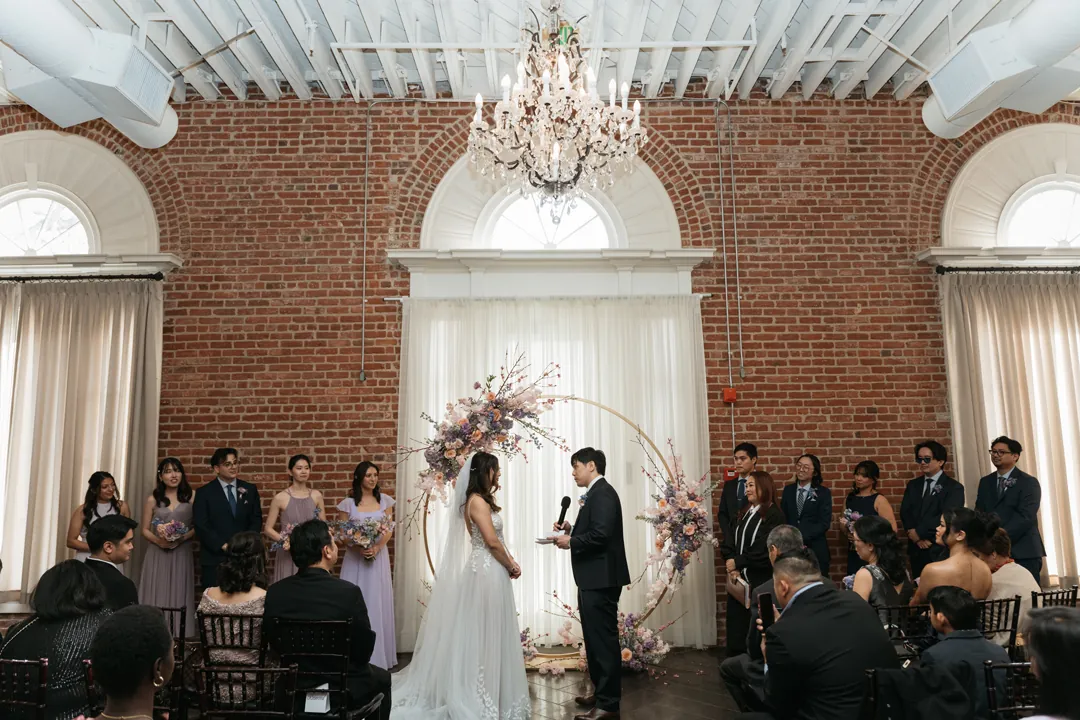 Guests watching a wedding ceremony beneath chandeliers