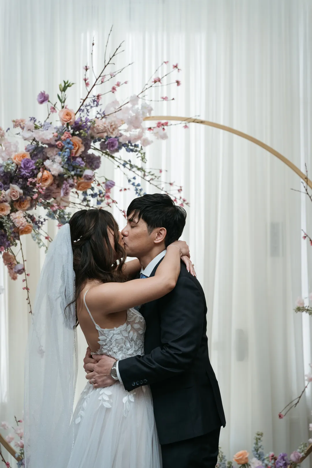 Couple kissing in front of a circular floral arch