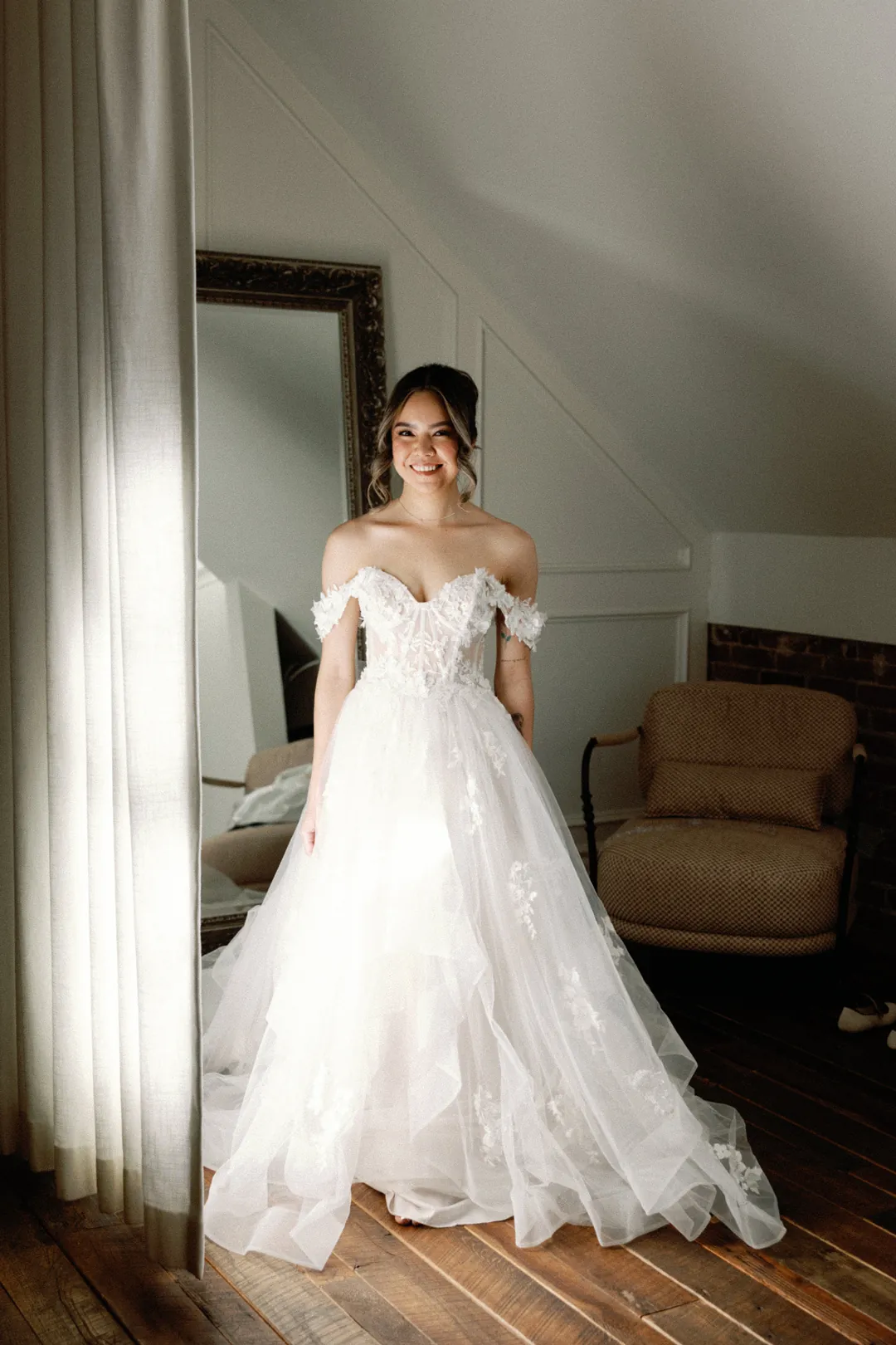 Bride standing near a loft window in a lace gown
