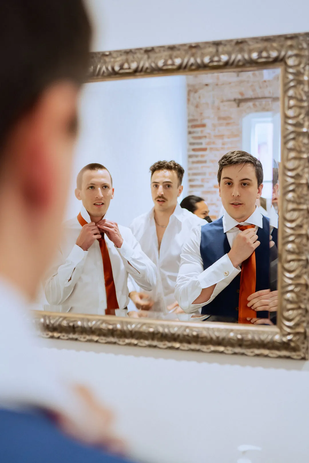 Groom and attendants adjusting their ties in a mirror