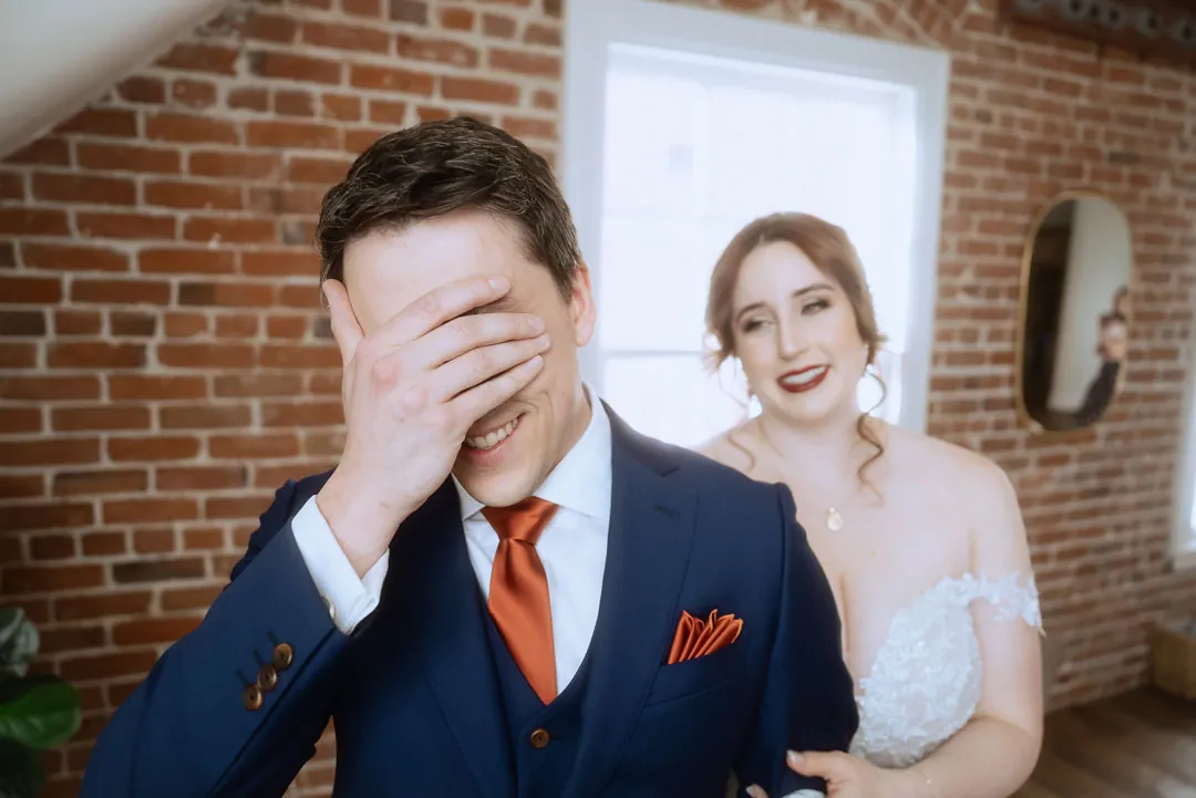 Groom covering his eyes as the bride approaches from behind