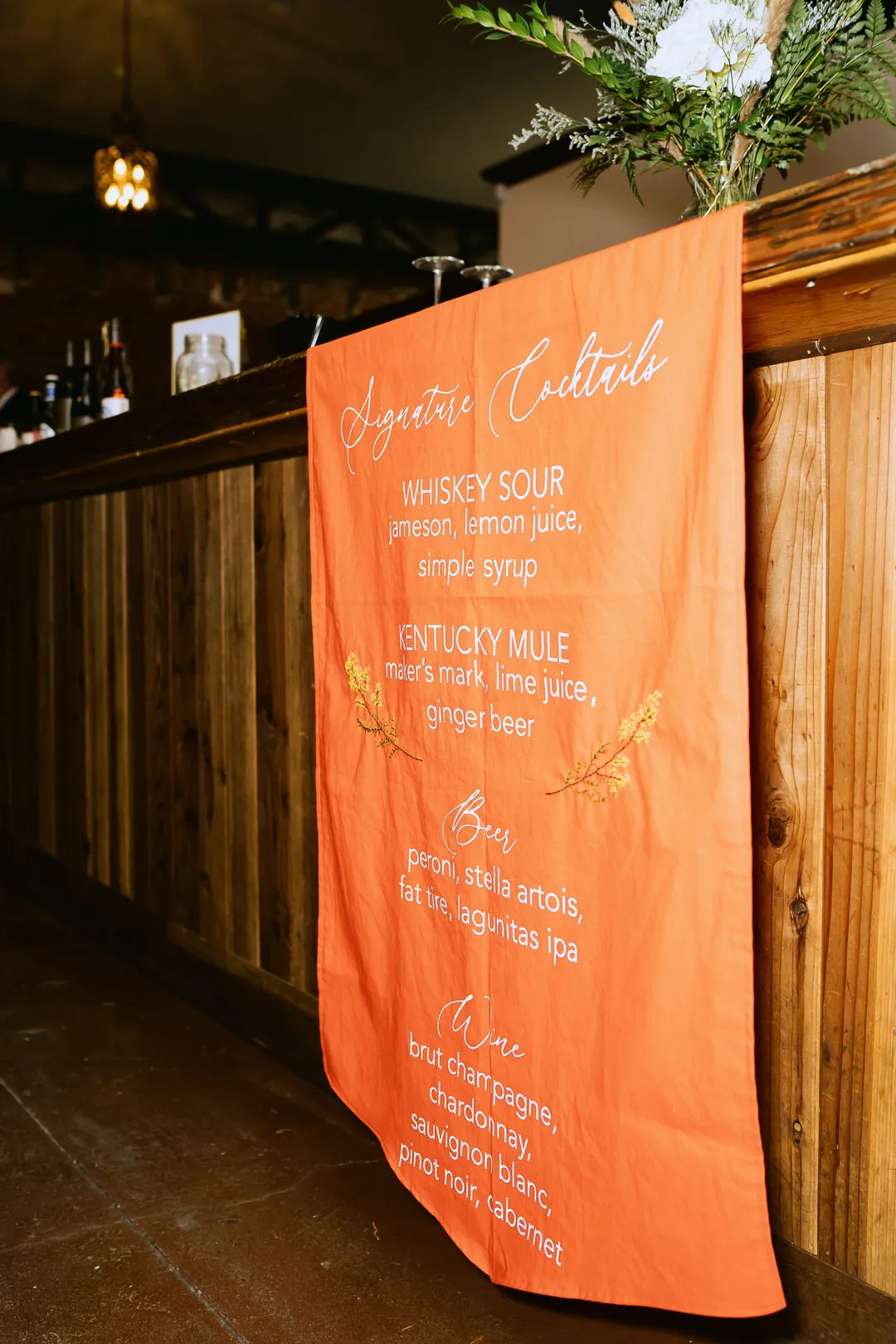 Orange wedding seating chart hanging at a bar