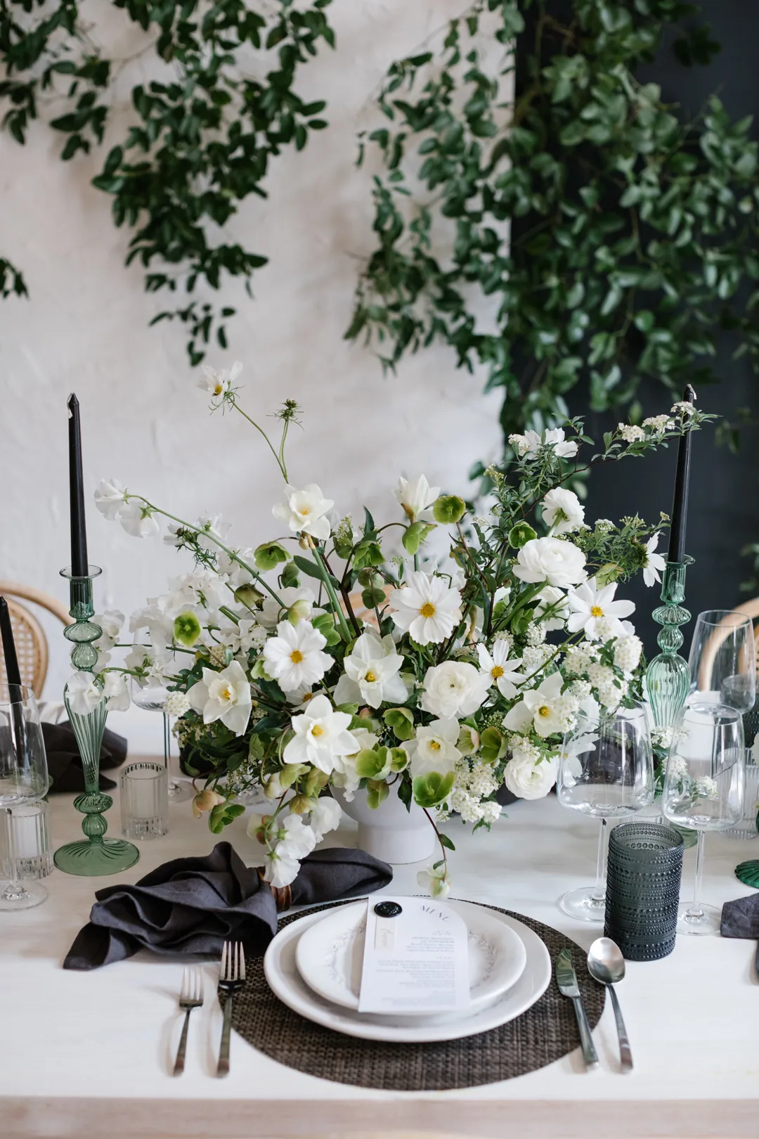 Floral centerpiece beside white plates and black napkins