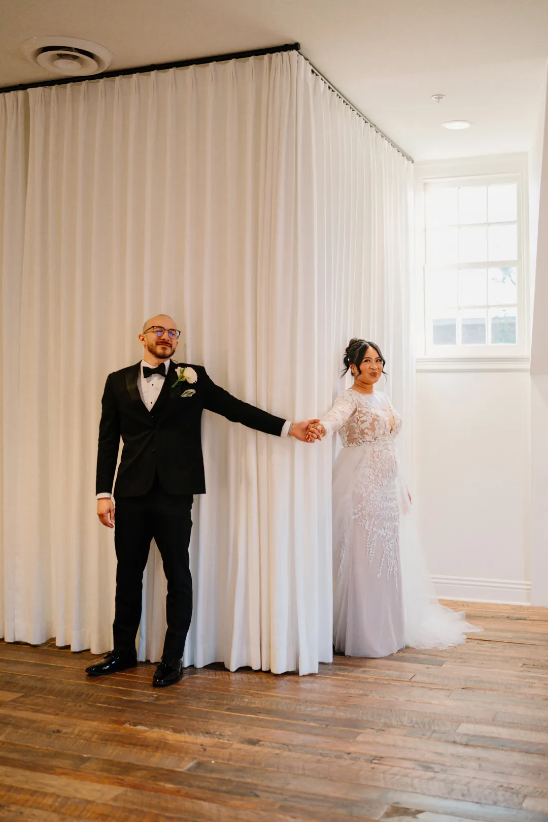 Couple holding hands beside pale curtains