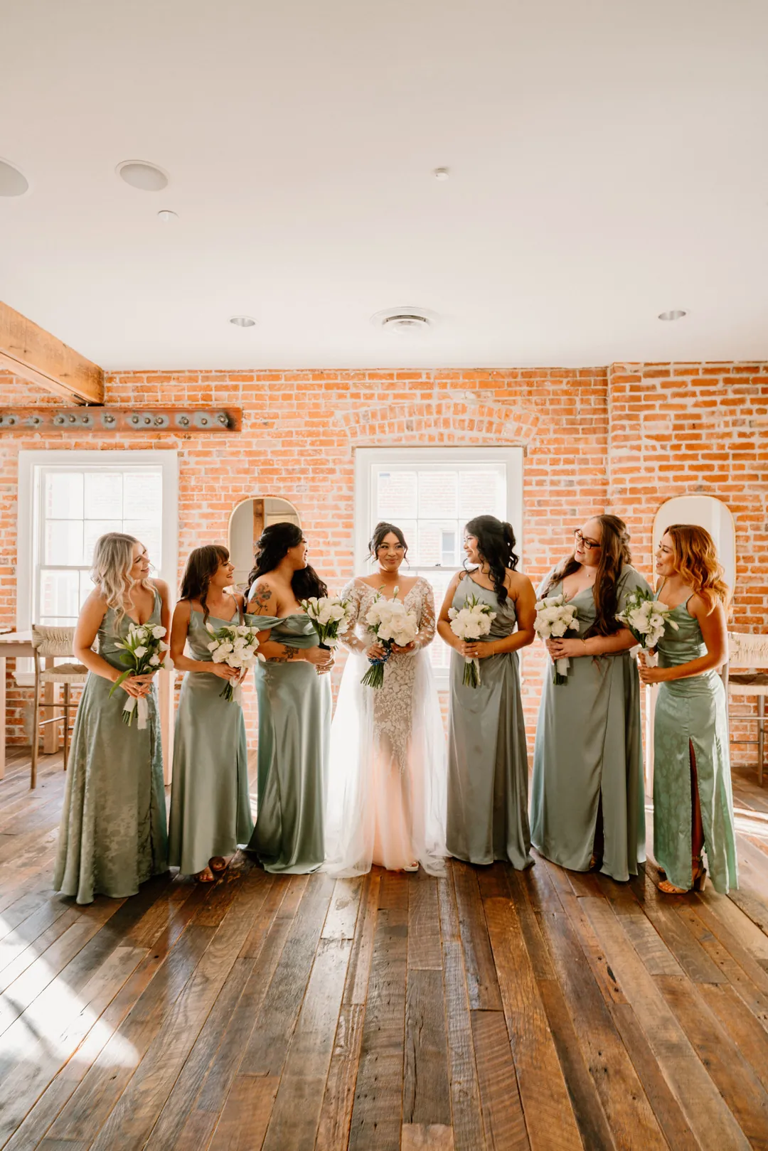 Bride and bridesmaids holding bouquets beside tall windows