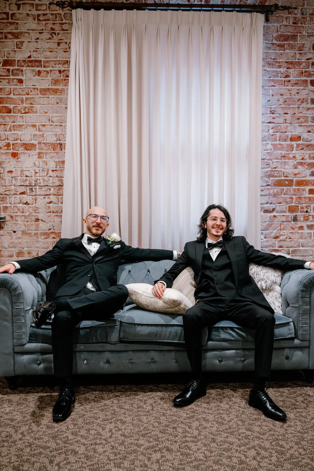 Groom and attendant seated on a dark sofa