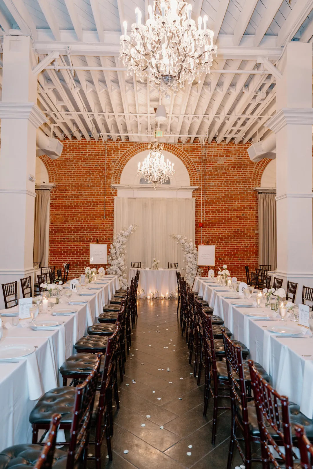 Long reception tables beneath chandeliers and an arched window