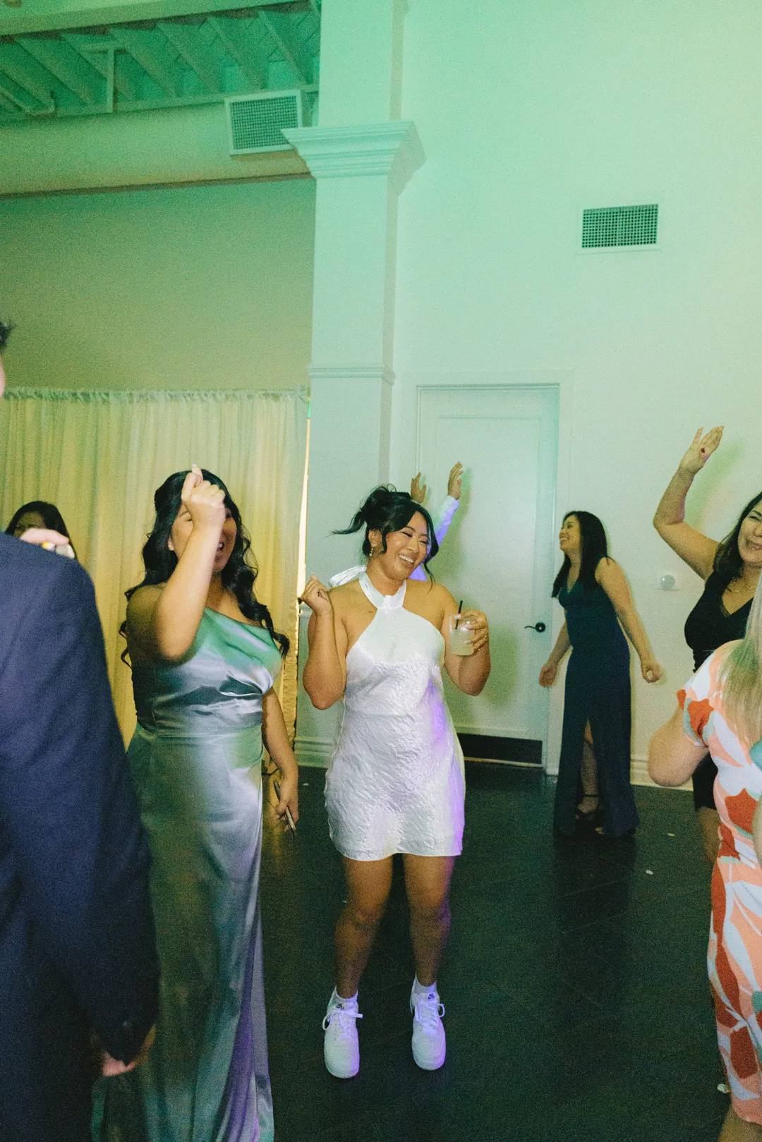 Guests dancing with their arms raised beneath green uplighting