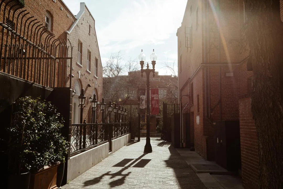 Sunlit outdoor walkway beside a brick building and iron fence