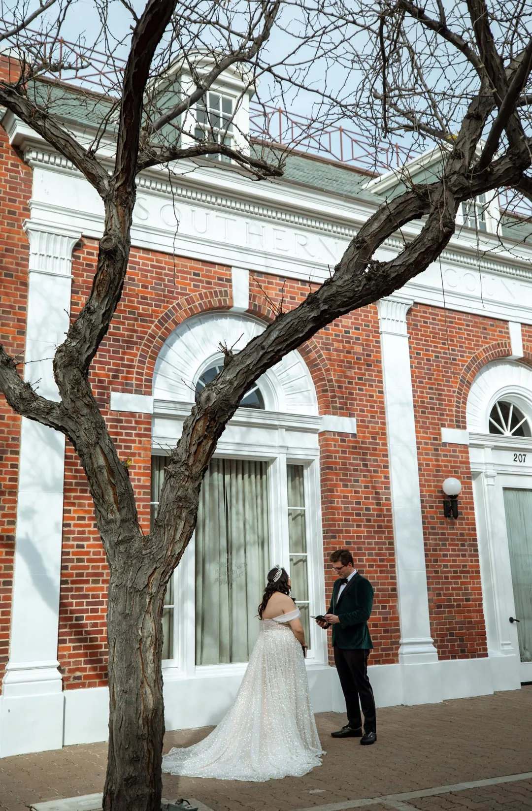 Couple standing beneath a tree beside a brick building