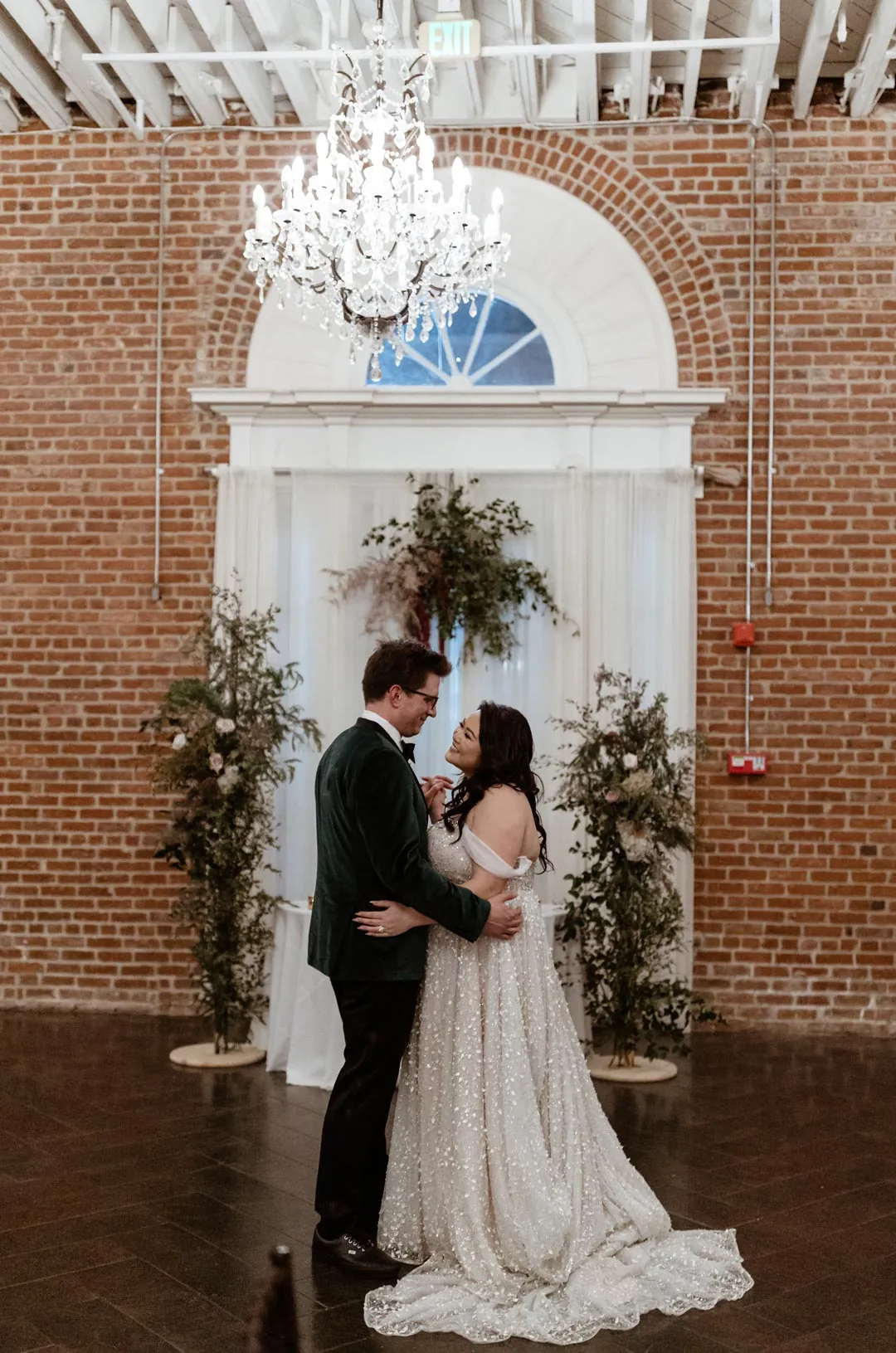 Couple dancing beneath a chandelier in front of an arched window
