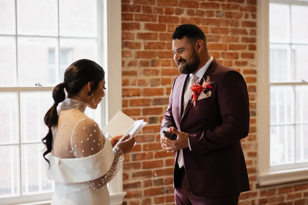 Couple exchange written vows beside a brick wall.