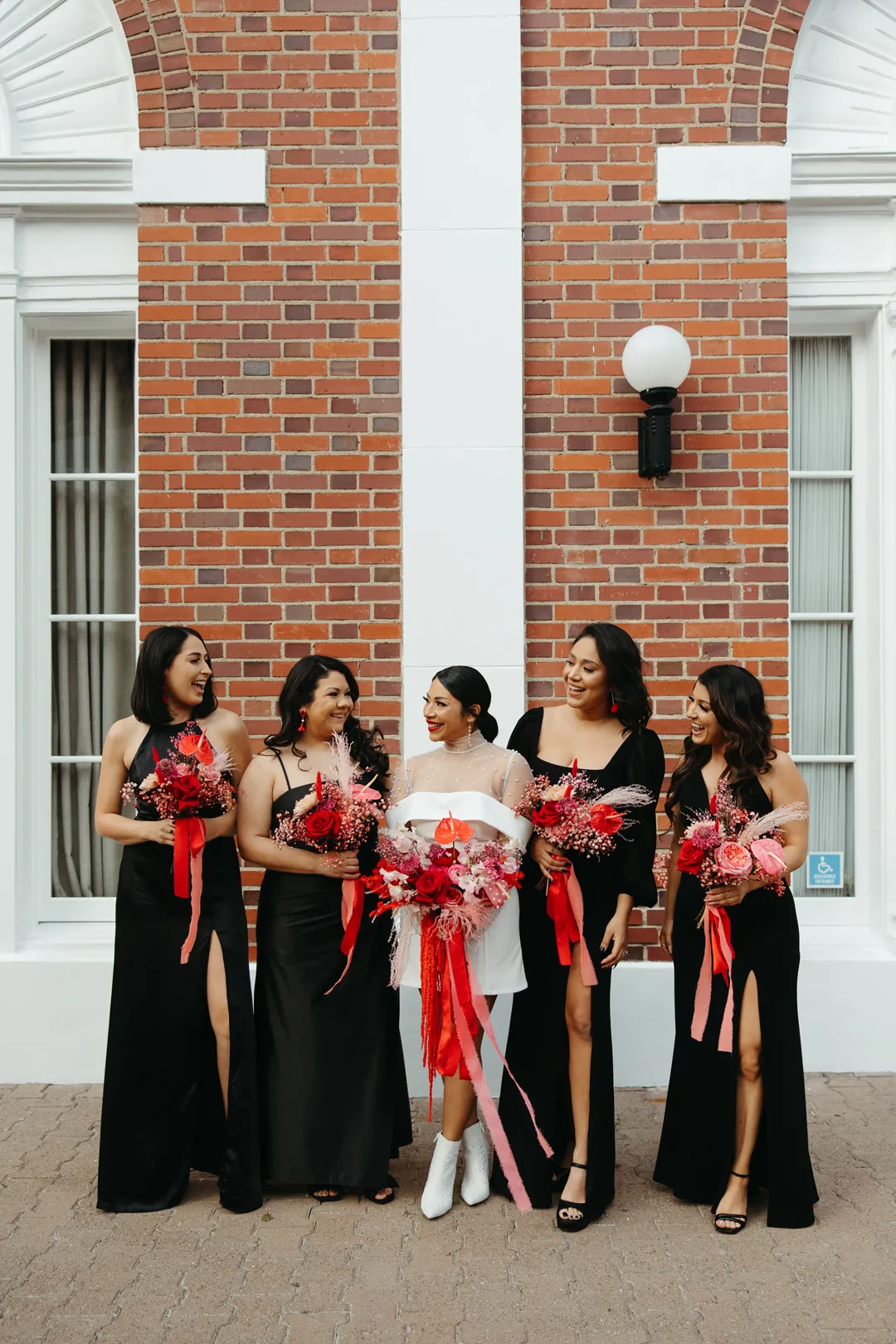 Bride poses with attendants holding red floral bouquets.
