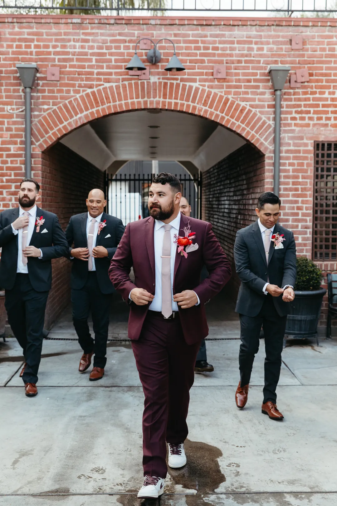 Groom and attendants walk out of a brick doorway.