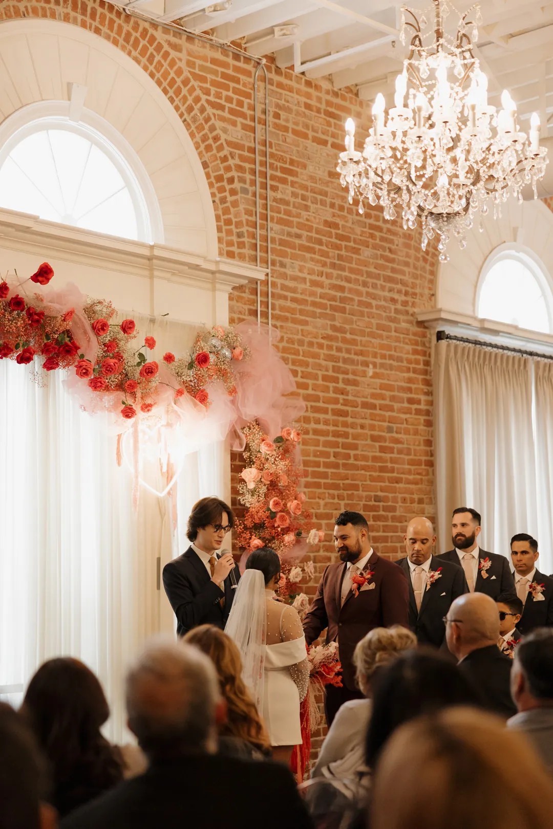 Wedding guests watch beneath a crystal chandelier.