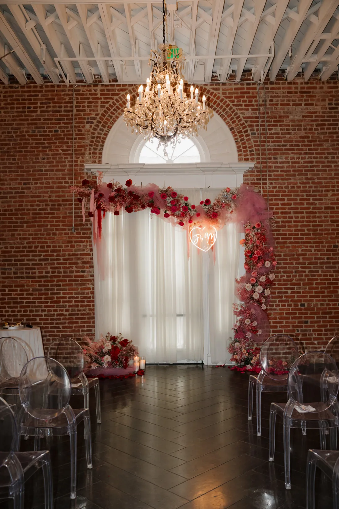 Red floral ceremony backdrop beneath a ballroom chandelier.
