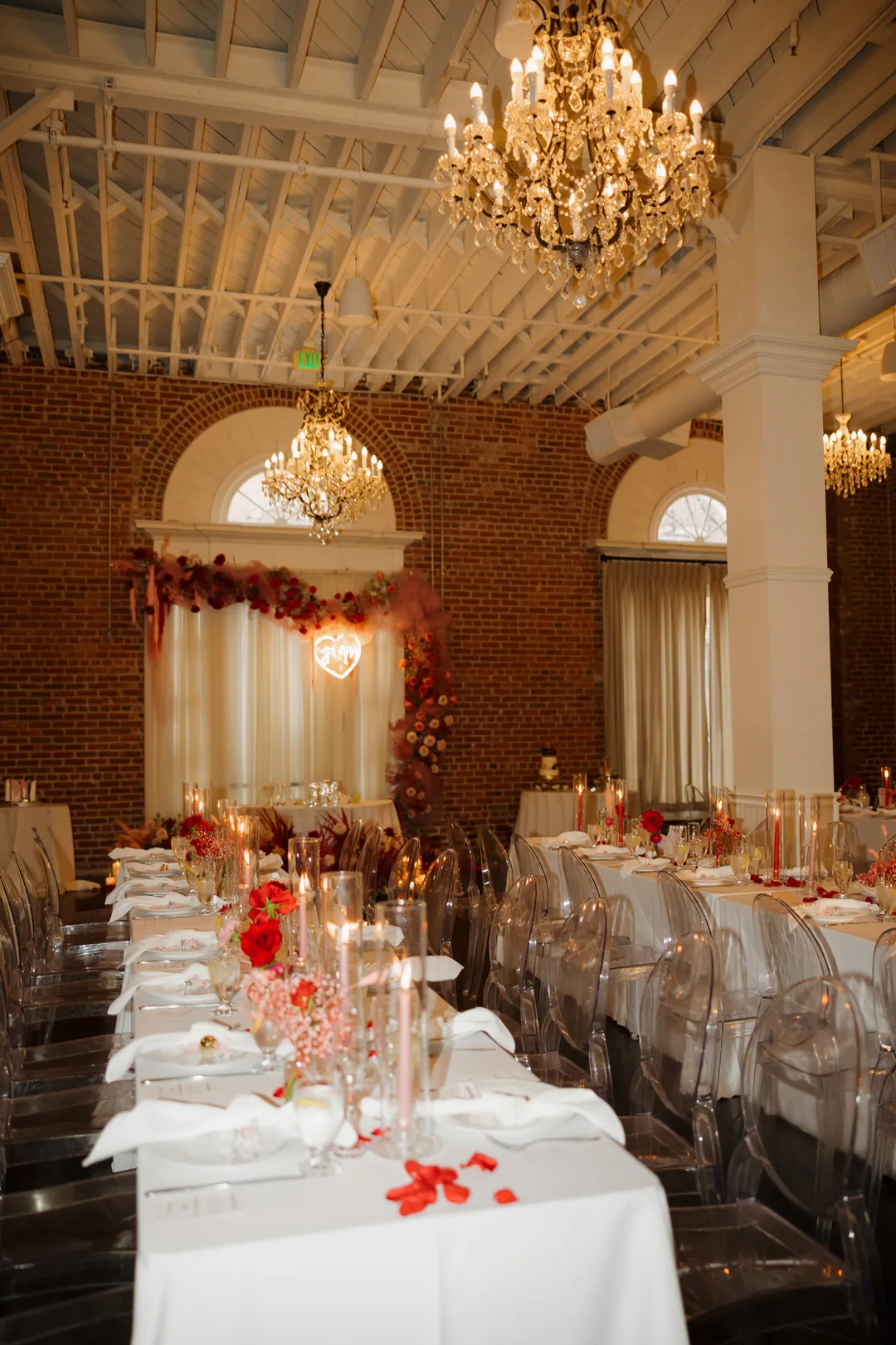 Reception tables decorated with flowers beneath chandeliers.