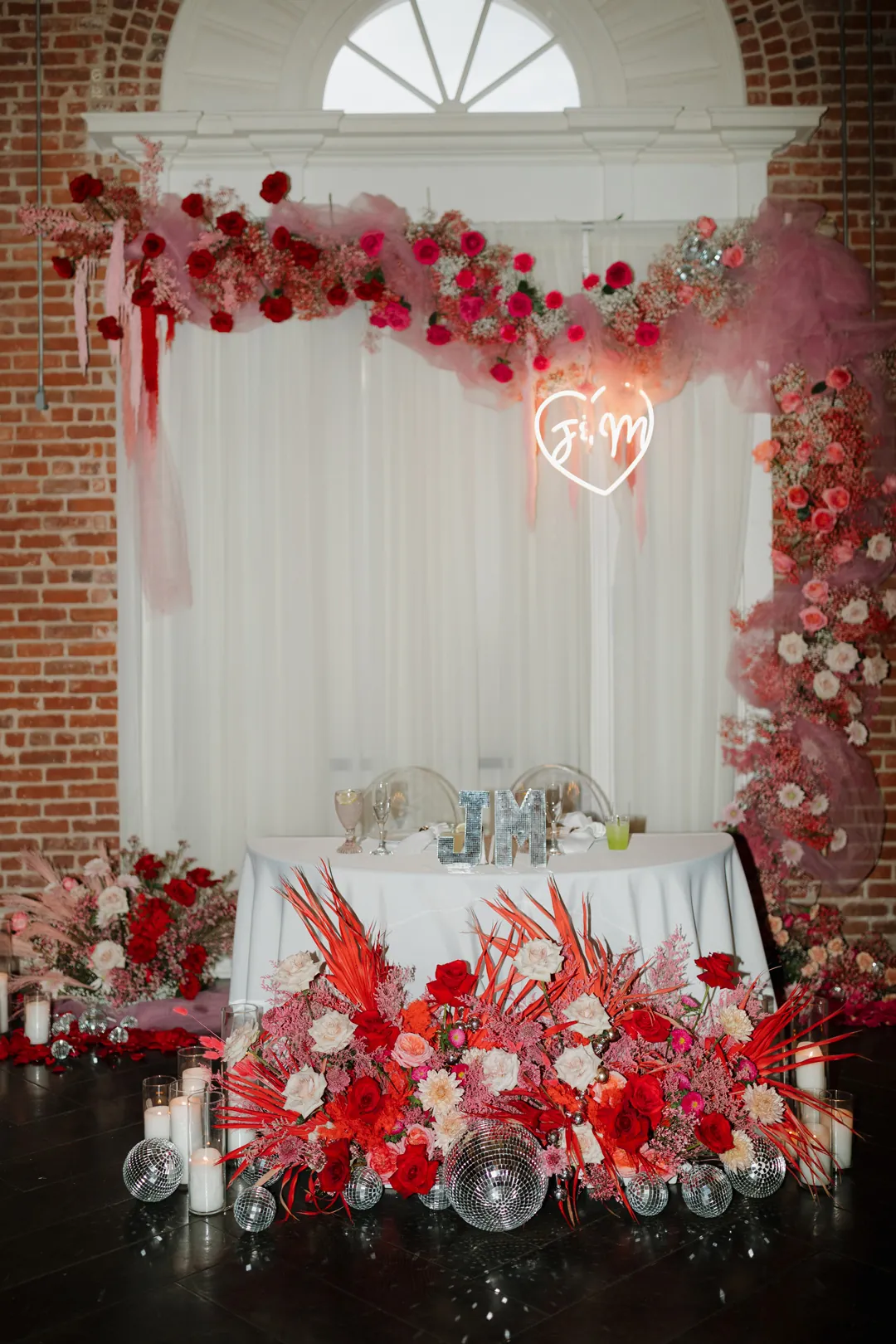 Red floral sweetheart table before a draped backdrop.