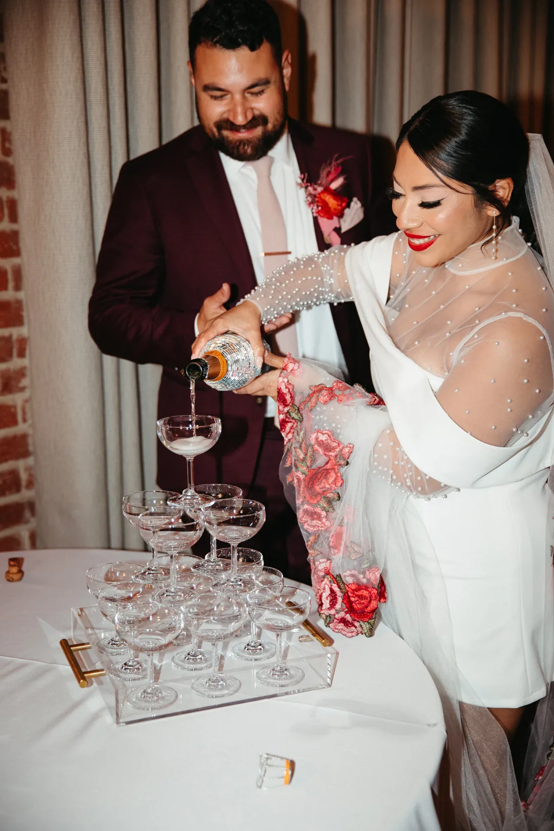 Bride pours a drink into stacked champagne glasses.