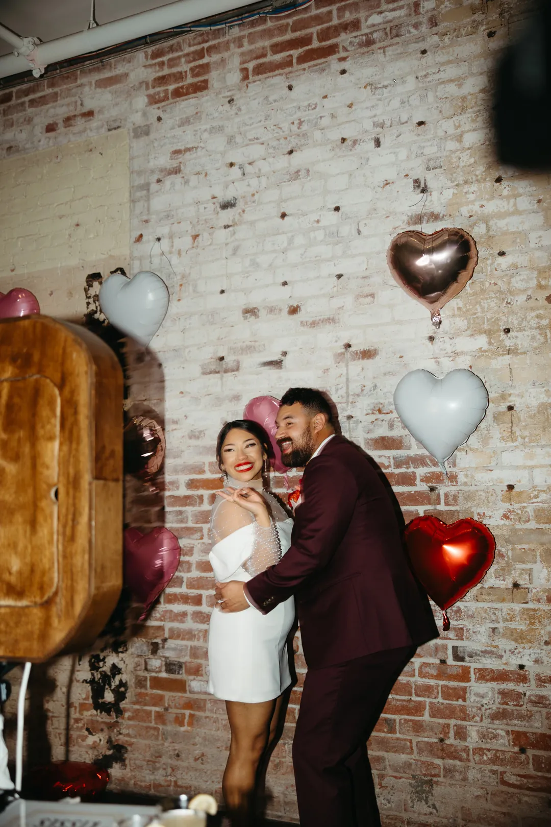 Couple kiss beside a wooden photo booth and balloons.