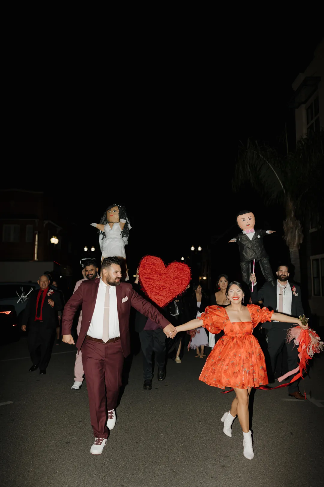 Newlyweds run outdoors with wedding guests at night.