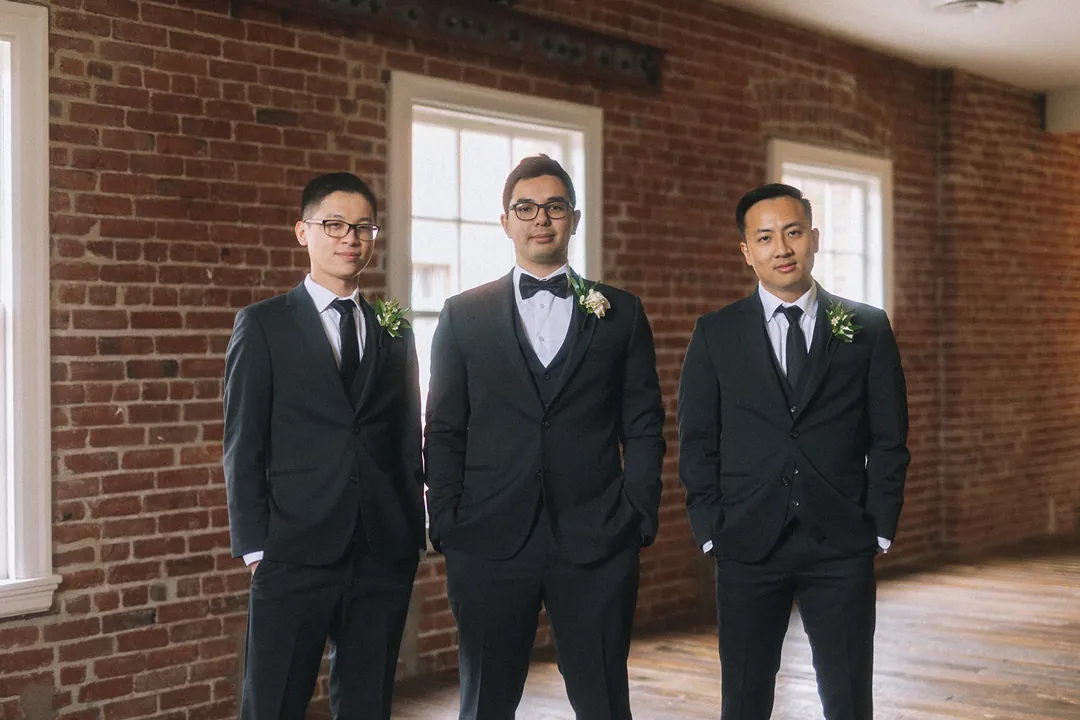 Groom posing with two attendants in dark suits