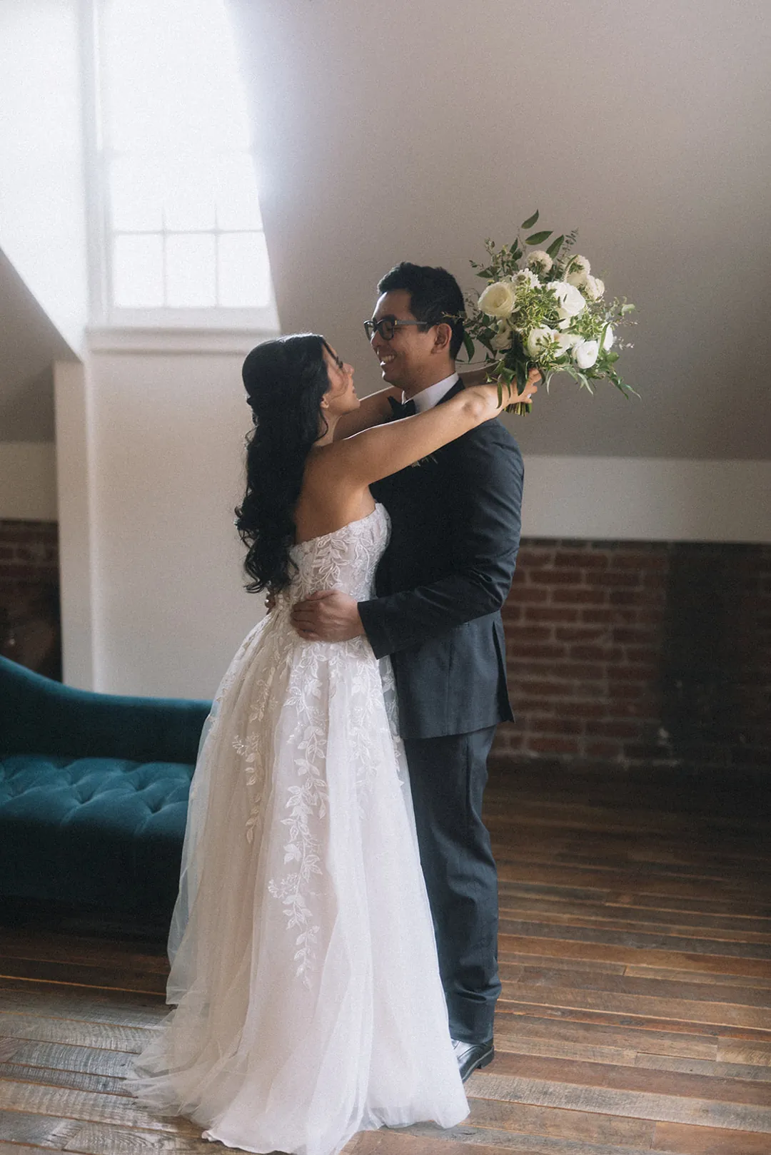 Bride and groom embracing beside a tall window