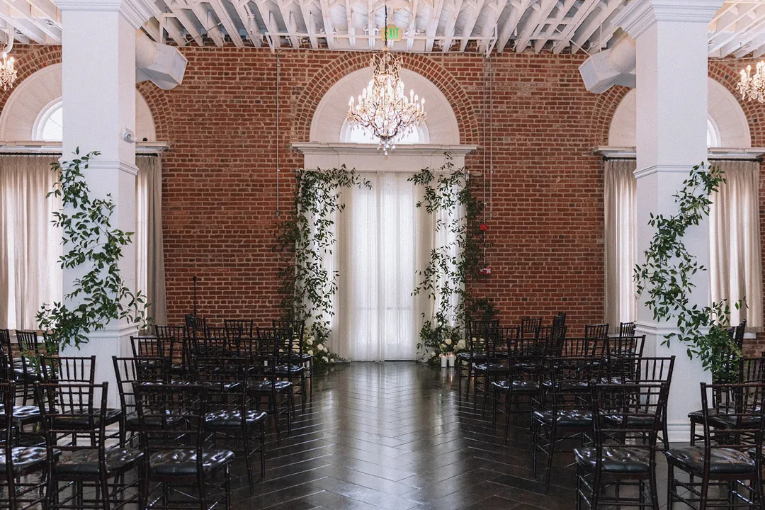 Rows of black ceremony chairs beneath chandeliers