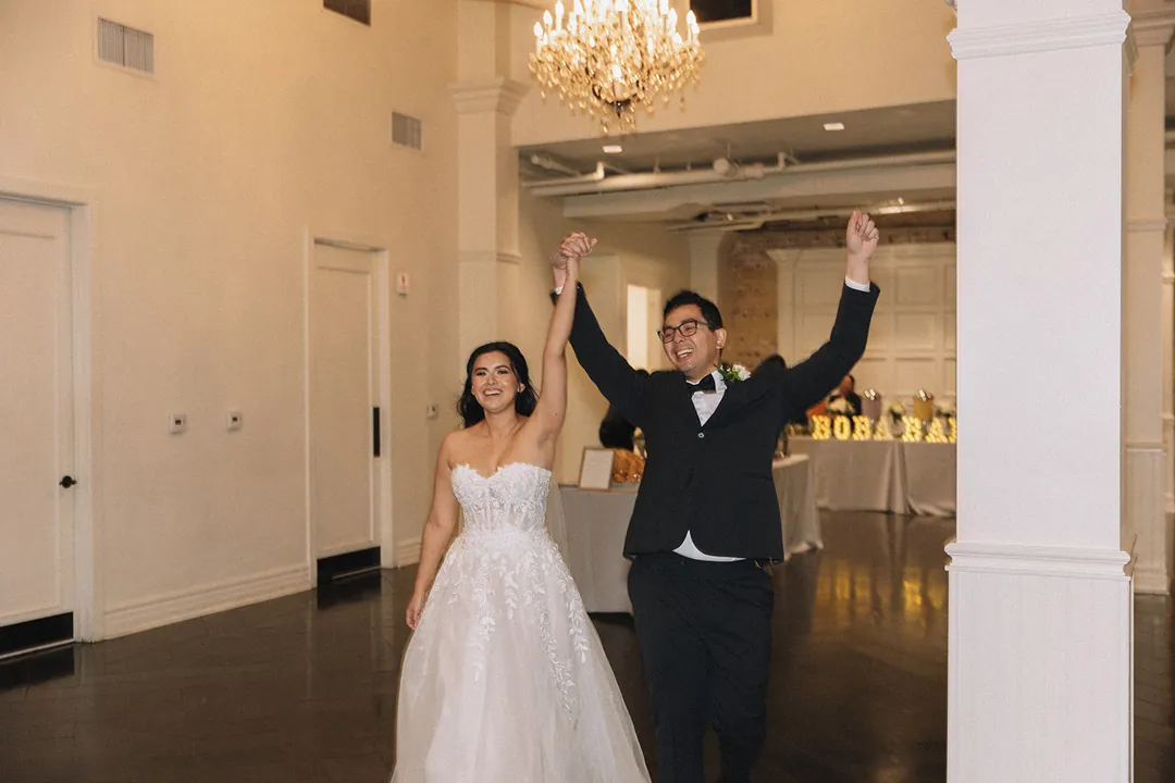 Newlyweds entering the reception with raised arms