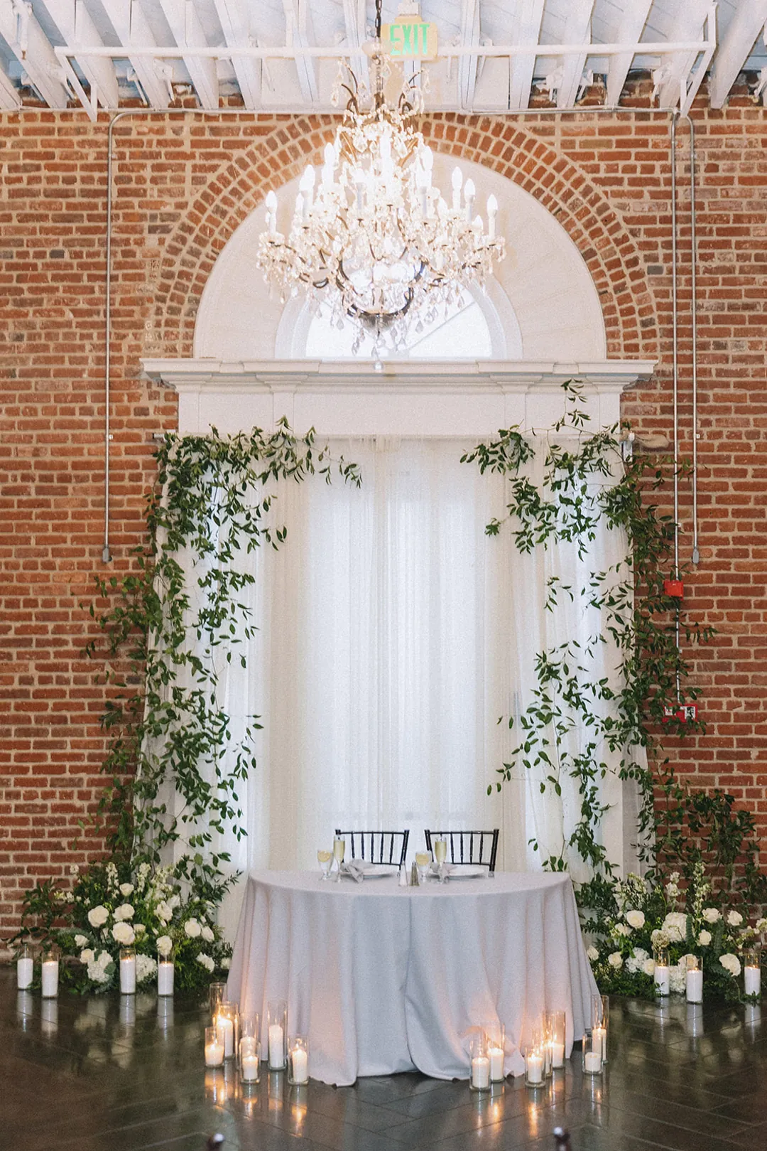 Sweetheart table beneath greenery and candlelight
