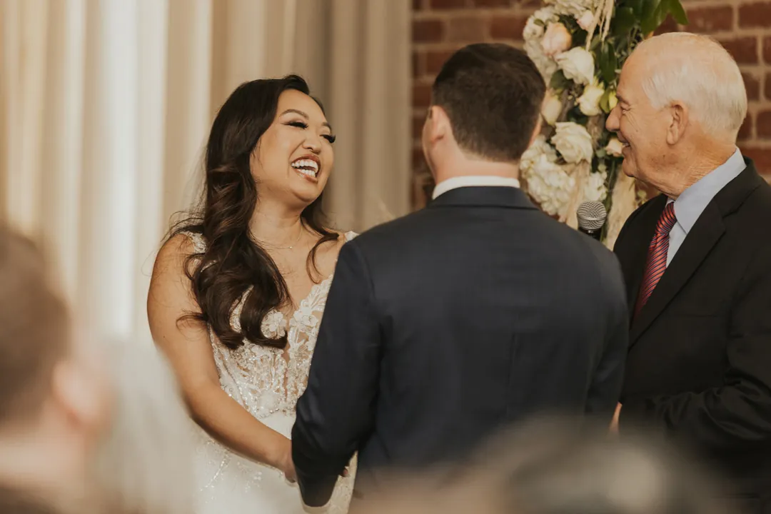 Bride laughs while facing the groom and officiant.