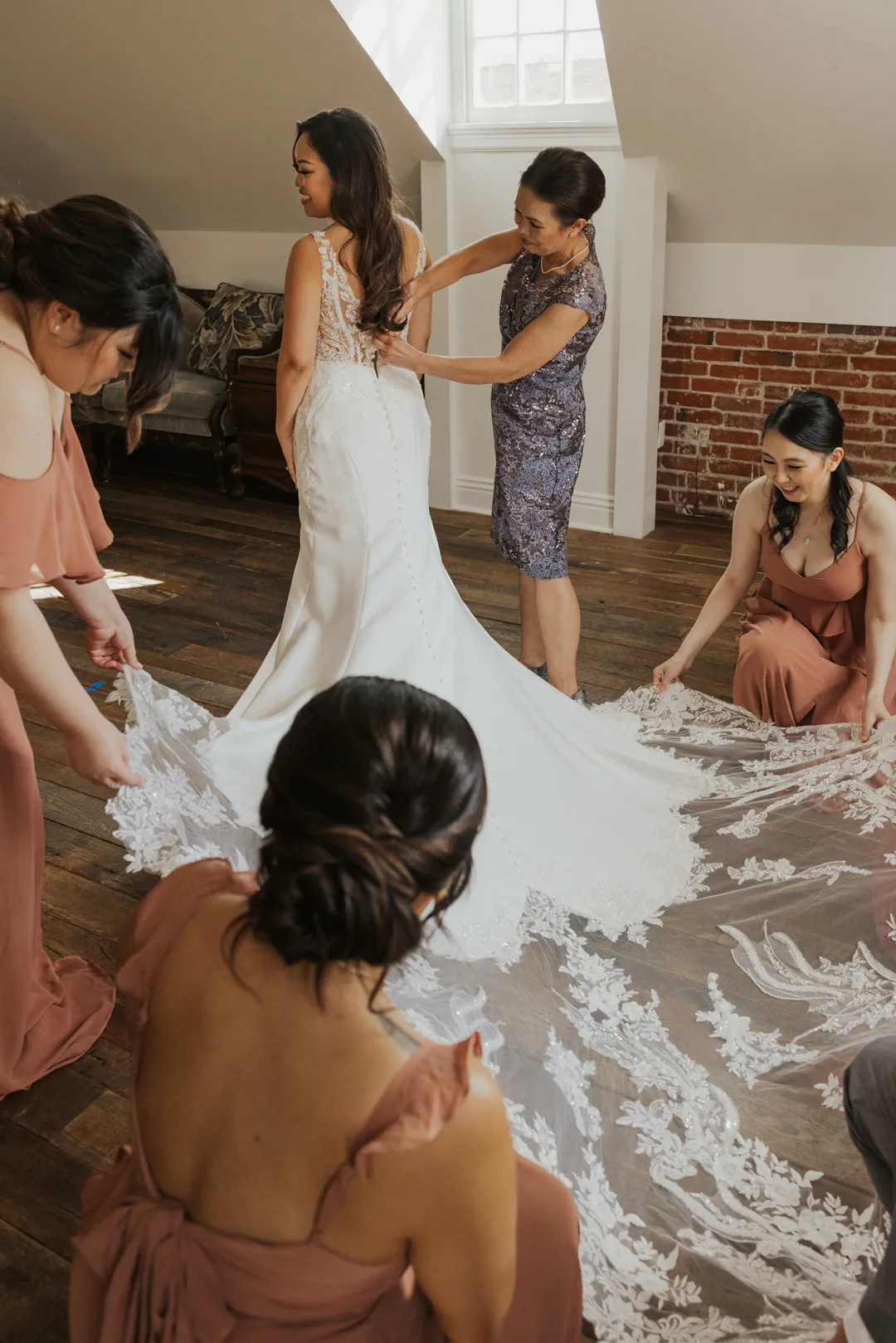 Attendants arrange the bride's long train in a loft room.
