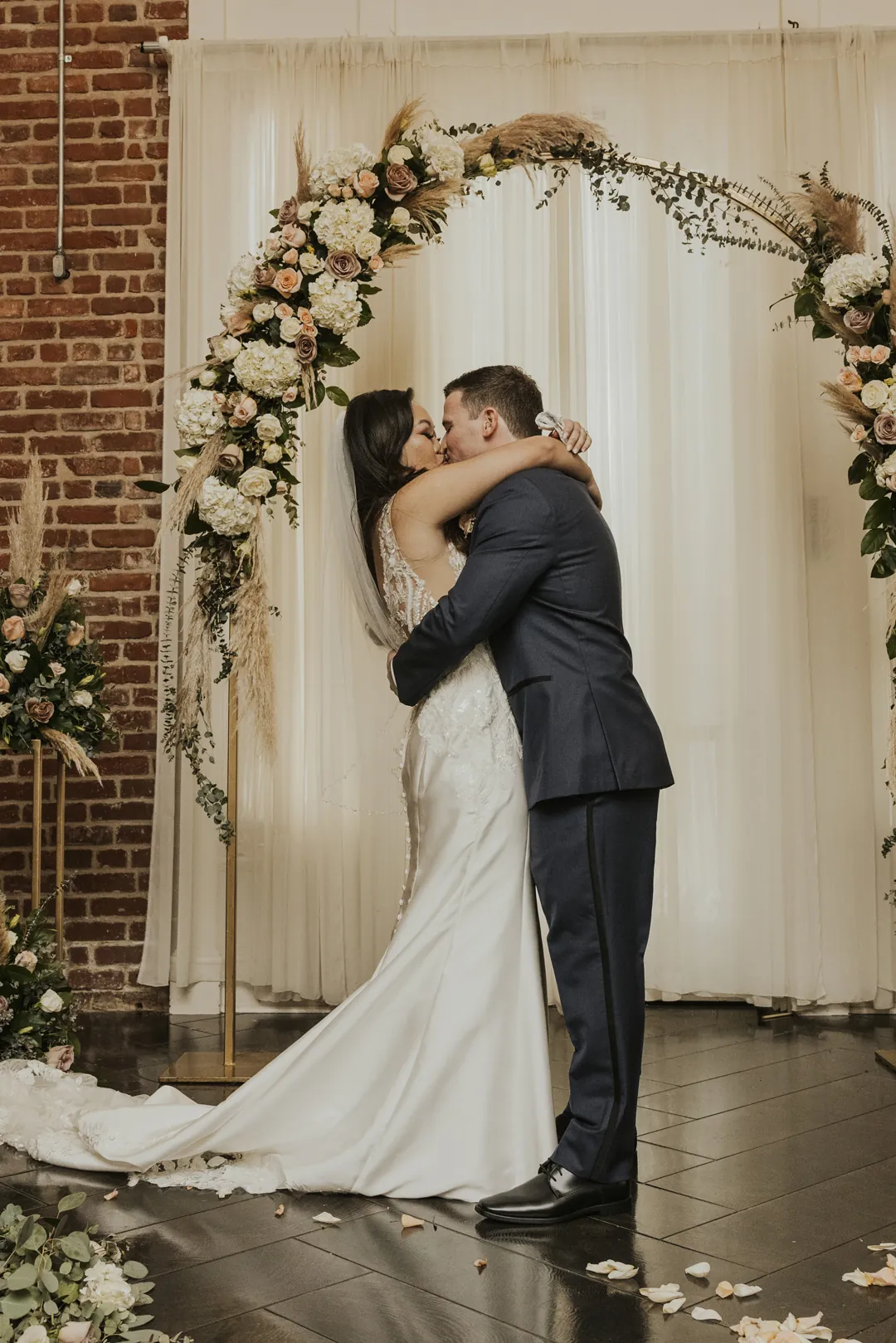 Newlyweds kiss beneath their floral ceremony arch.