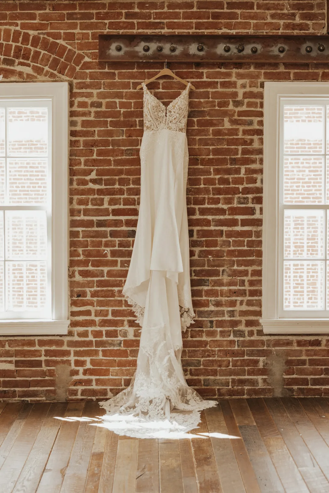 Lace wedding dress hangs between two loft windows.