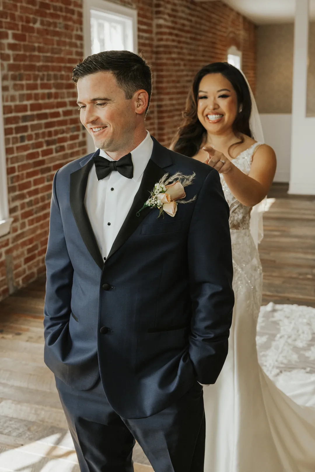 Bride approaches a smiling groom from behind.