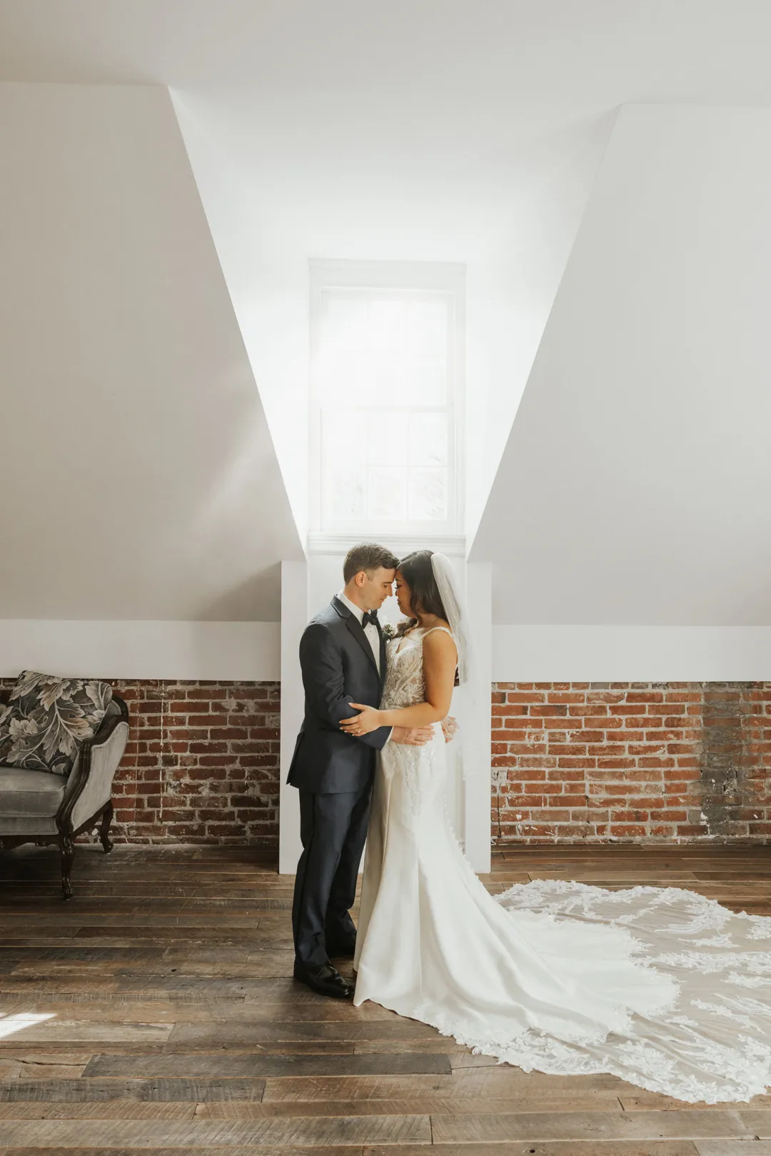 Couple embrace in a sunlit loft beneath an angled ceiling.
