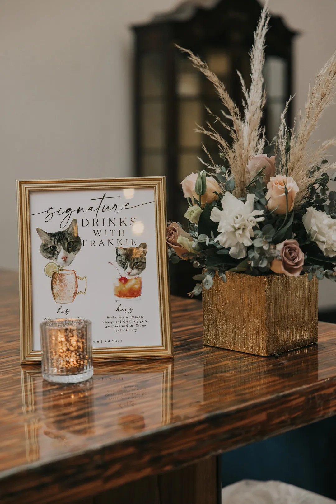 Framed cocktail menu beside a dried floral arrangement.