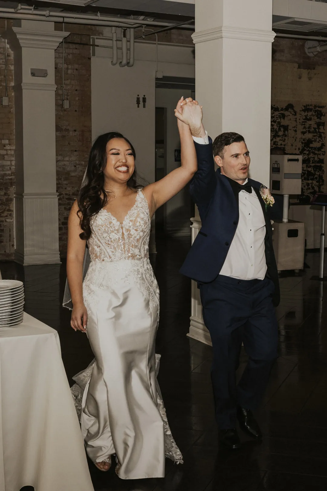 Newlyweds enter their reception with joined hands raised.