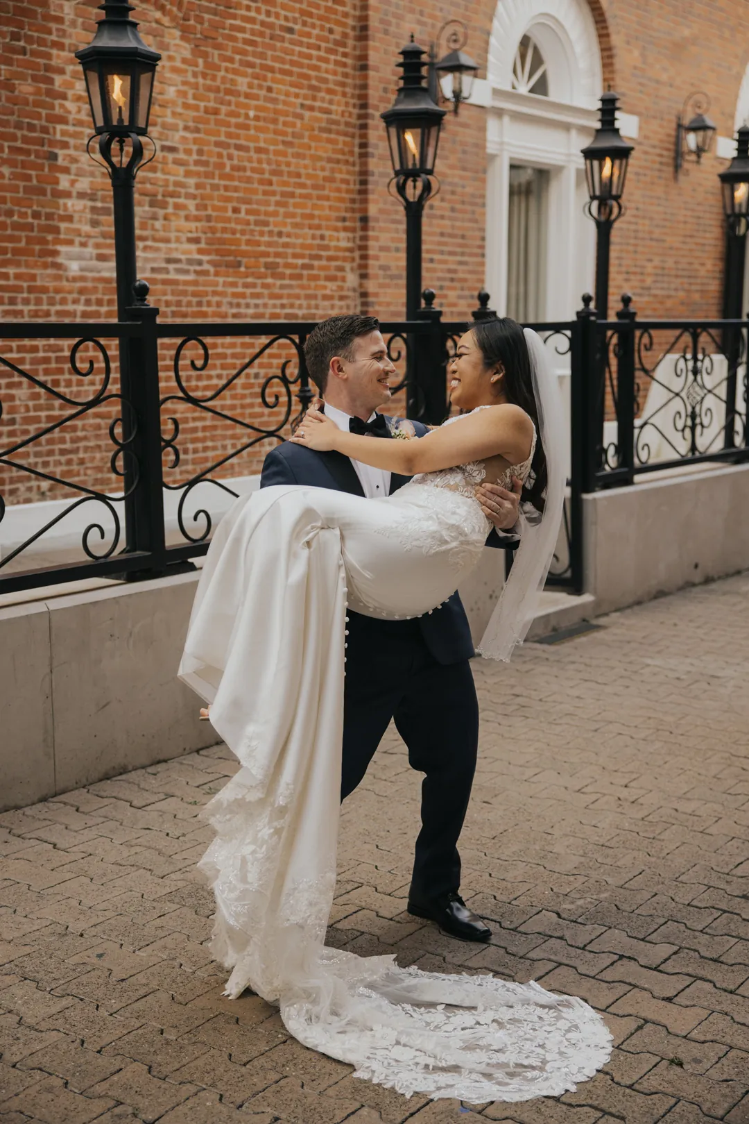 Groom carries the bride along a brick paved walkway.