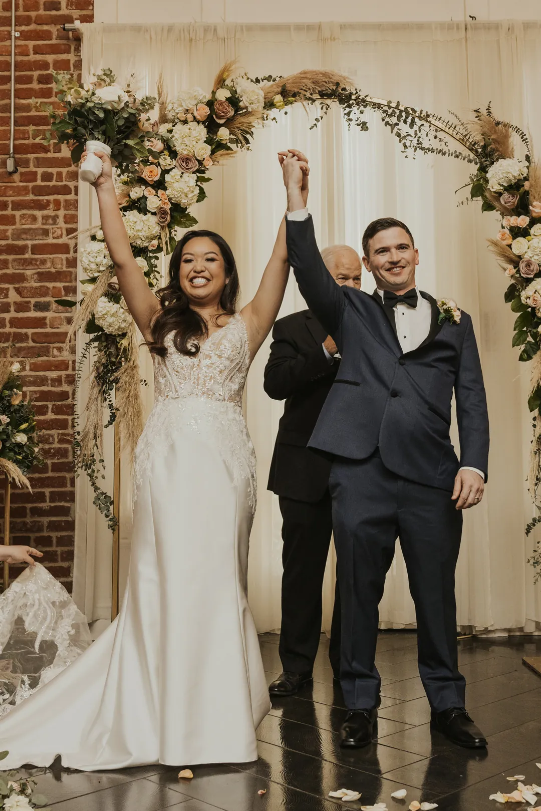 Newlyweds raise joined hands before their ceremony backdrop.