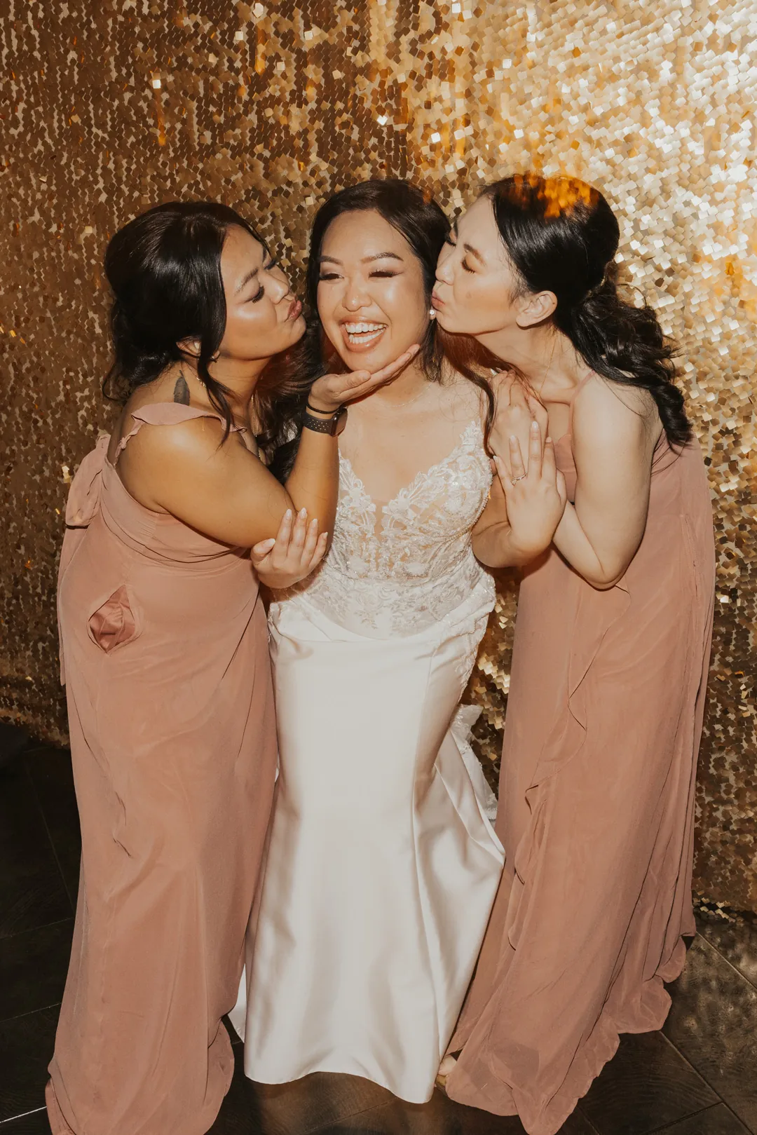 Bride poses with attendants against a gold backdrop.
